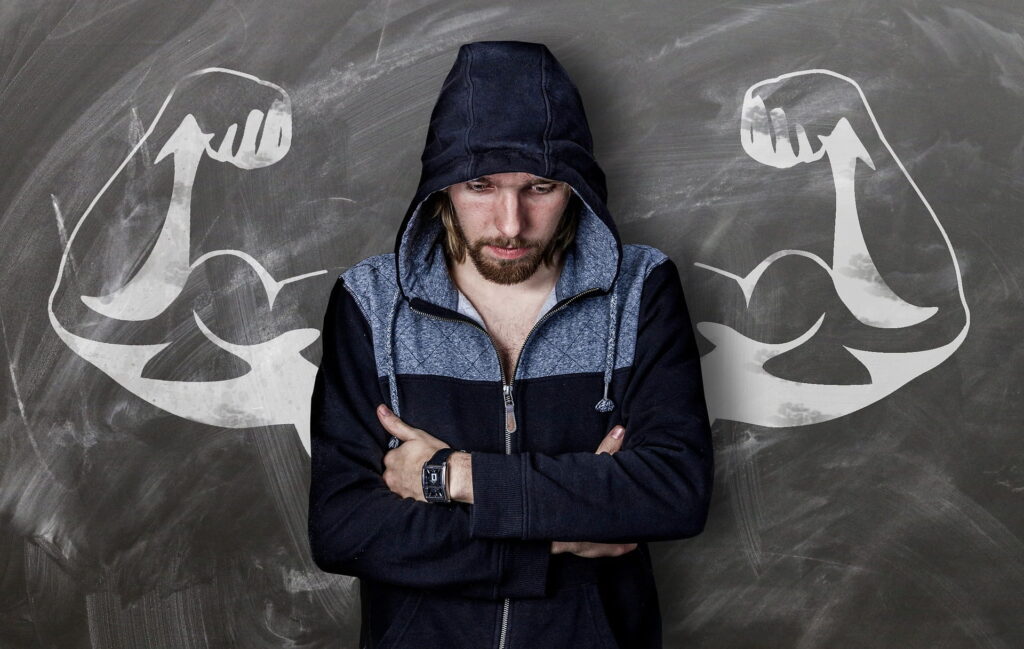 A man in a hoodie standing with muscular arms drawn behind him, symbolizing his goal of gaining muscle mass.