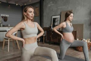 Two women working out together, one postpartum and the other pregnant, engaging in a safe pregnancy workout plan.