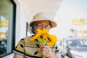 Happy elderly woman smelling flowers, highlighting the importance of meeting nutritional requirements for elderly people.