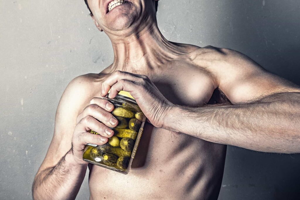 Muscular man struggling to open a jar, symbolizing strength and energy associated with high testosterone levels