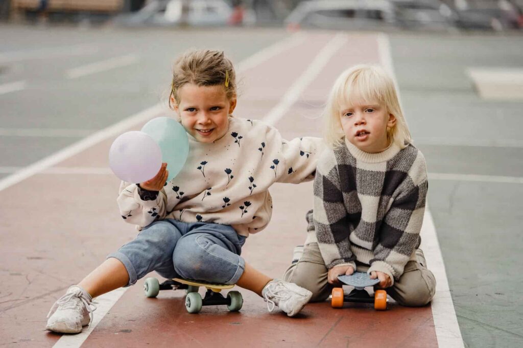 two children sitting on skateboards on a track