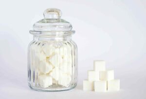 how many grams of sugar should you eat a day - glass jar filled with sugar cubes and a small pyramid of sugar cubes next to it on a white background