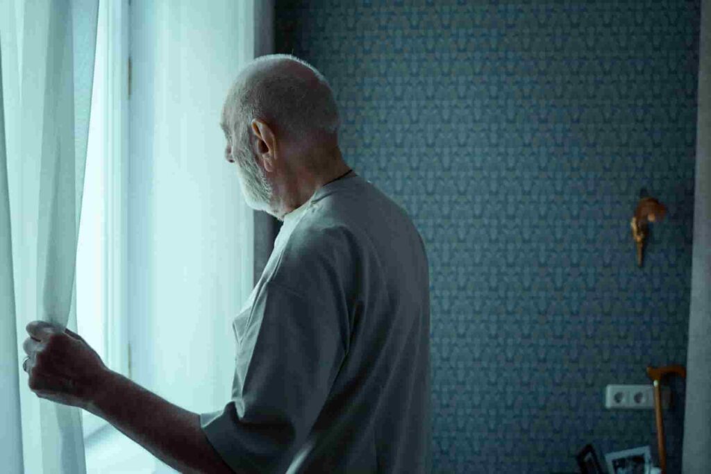 An elderly man with chronic fatigue stares out the window